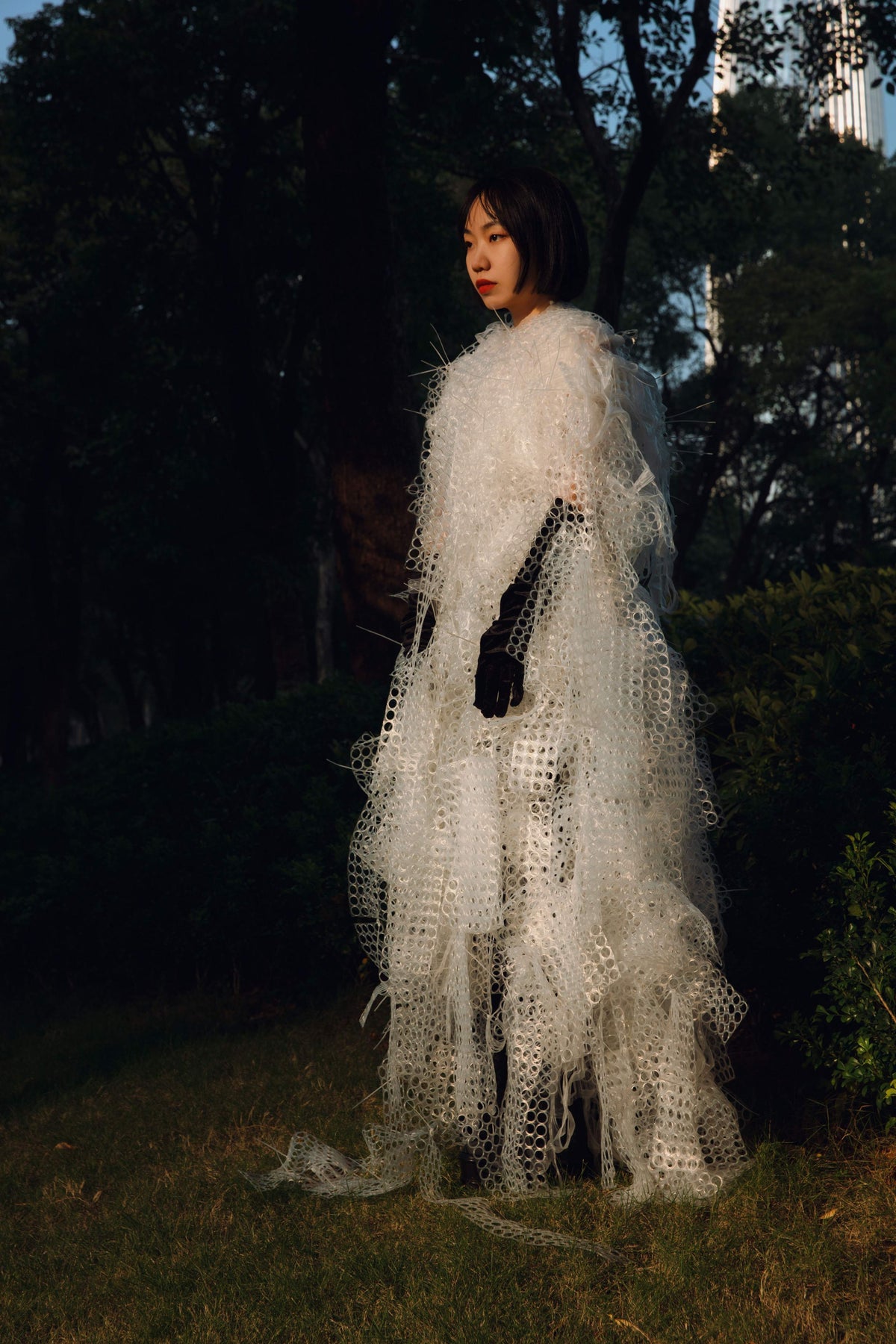 Yuling Yu wearing a work made from discarded rubber netting in a dark forest